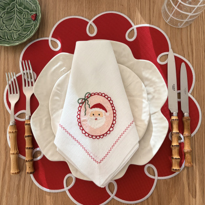 Mesa posta com pratos brancos, guardanapo com bordado de Pai Natal, talheres com cabos de bambu e placemat vermelho