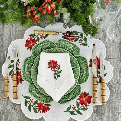 Mesa posta com decoração de flores vermelhas, pratos verdes e talheres com cabos de madeira clara