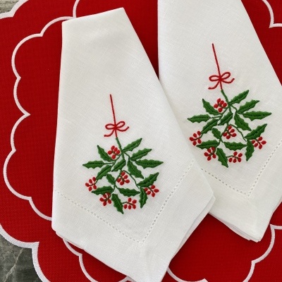 Duas guardanapos brancos bordados com azevinho sobre base vermelha com contorno branco