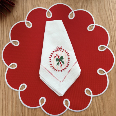 Jogo americano vermelho com bordas brancas e guardanapo branco bordado com motivo natalício