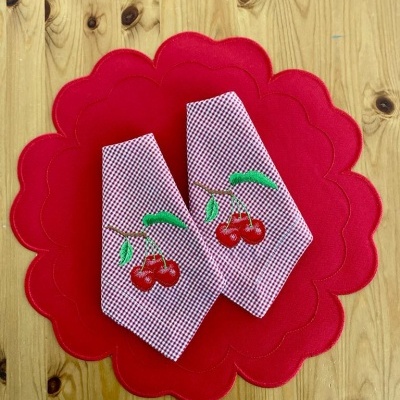 Panos de cozinha com estampa de cerejas sobre toalhete vermelho ondulado, em madeira clara