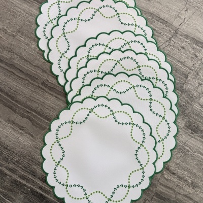 Bases de mesa ovais brancas com bordas verdes e bordados em verde sobre superfície cinza.