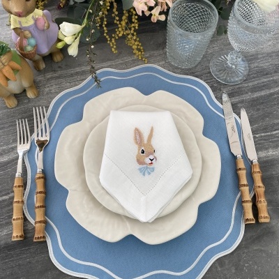 Mesa posta com pratos brancos, guardanapo bordado, talheres com cabo de madeira e decoração de Páscoa