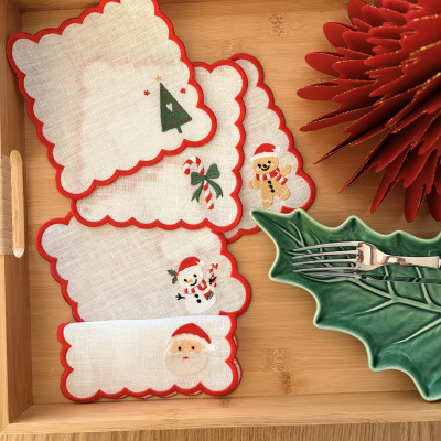 Guardanapos de Natal de tecido branco com bordas vermelhas e desenhos natalícios sobre tabuleiro de madeira.