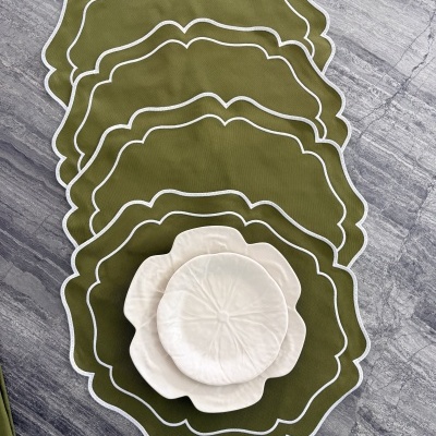 Individual de mesa verde-oliva com pratos brancos em forma de flor sobre pedra cinzenta