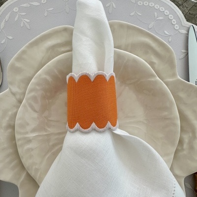 Pratos de cerâmica bege com guardanapo branco e anel de tecido laranja sobre toalha branca com padrão floral