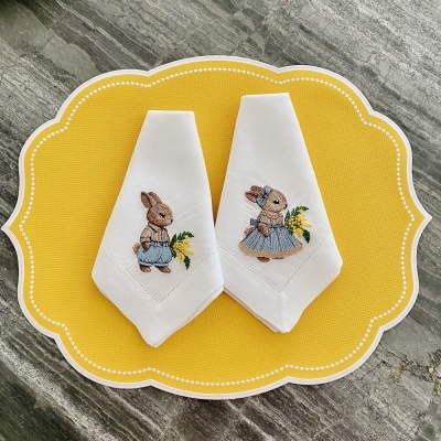 Dois guardanapos de pano com bordados de coelhos sobre sousplat amarelo