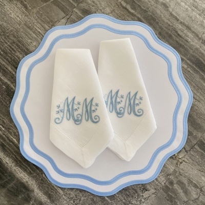 Guardanapos brancos bordados com letras azuis sobre prato branco com borda azul