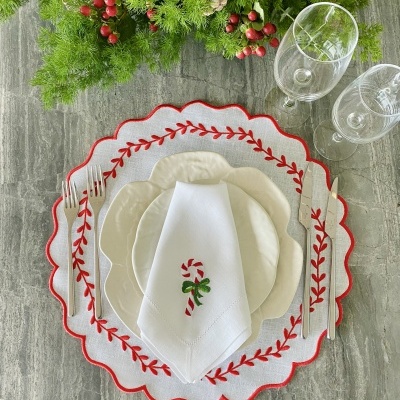 Conjunto de mesa natalício com prato branco, sousplat bordado vermelho, guardanapo com bengala de natal e talheres ao lado
