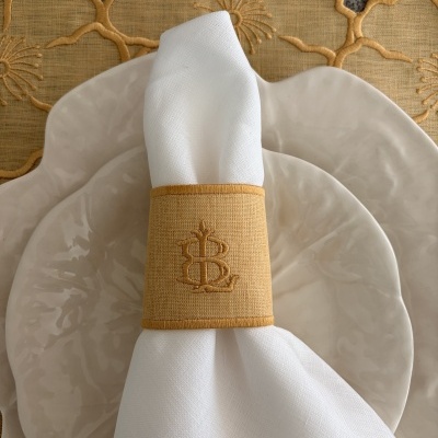 Conjunto de loiça com pratos cerâmicos creme, guardanapo branco com argola bordada amarela e toalha floral amarela.