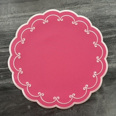 Individual redondo de tecido vermelho com bordado branco em arabescos sobre fundo de mármore cinza.