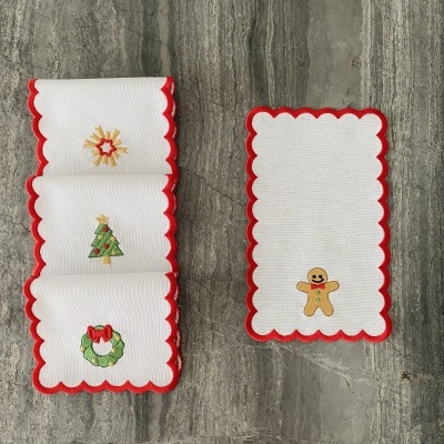 Toalhetes brancos com bordas vermelhas e bordados de Natal, como árvore, estrela, coroa e boneco de gengibre.