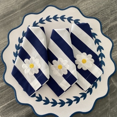 Guardanapos riscas azuis e brancas com flor bordada sobre prato branco com padrão azul