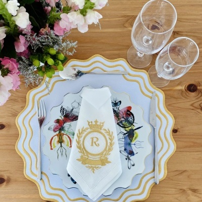 Conjunto de jantar com pratos decorativos, guardanapo com monograma e dois copos em mesa de madeira