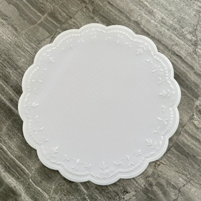 Toalha de mesa redonda branca com bordado de folhas e círculos em superfície de pedra cinza.