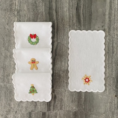 Guardanapos brancos com bordados de Natal e bordas onduladas numa superfície cinzenta