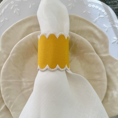 Guardanapo branco com anel amarelo sobre pratos bege e branco num fundo de madeira cinzenta