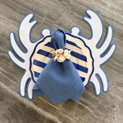 Conjunto de loiça com prato às riscas azuis e creme, guardanapo azul com argola de conchas, base em padrão coral azul e branco, superfície cinza