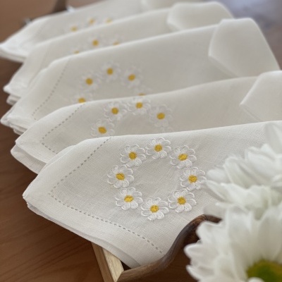 Toalhas brancas bordadas com flores amarelas e brancas numa caixa de madeira.