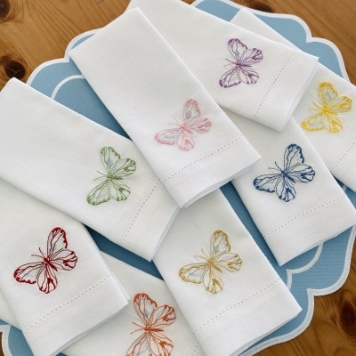 Guardanapos brancos com bordados coloridos de borboletas em prato azul sobre mesa de madeira