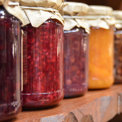 Frascos de compotas coloridas em vidro com tampas de papel pardo numa prateleira de madeira