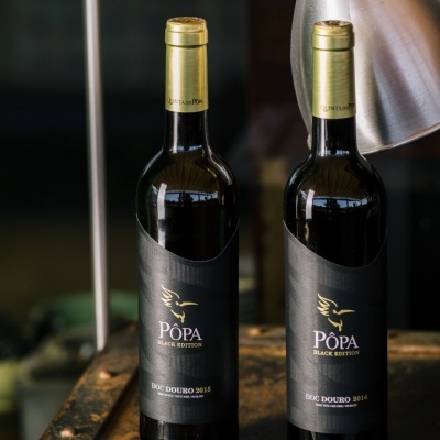 Duas garrafas de vinho tinto POPA Black Edition com rótulos pretos e tampas douradas em superfície metálica
