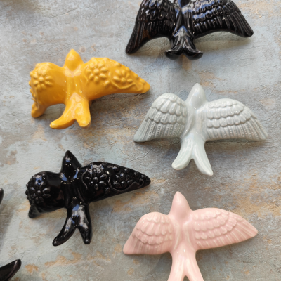 Figuras de cerâmica de pássaros coloridos com asas abertas sobre superfície cinza