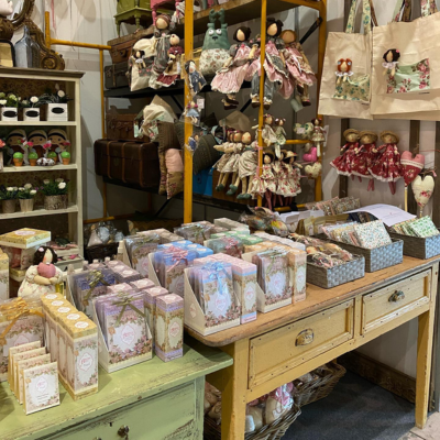 Produtos artesanais em mesa e estante de madeira com caixas e bonecas decorativas.
