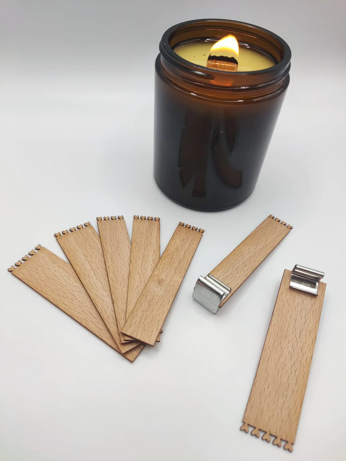 Vela acesa em frasco de vidro castanho com várias palhetas de madeira dentadas e duas com presilhas metálicas
