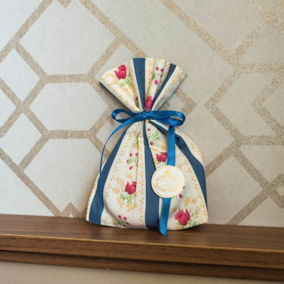 Saco de tecido com padrão floral e fita azul numa prateleira de madeira