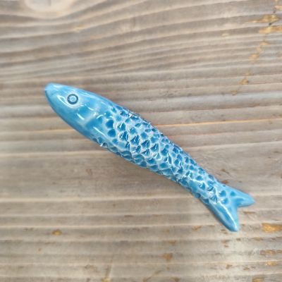 Peixe decorativo cerâmico azul com textura e olho pintado sobre madeira