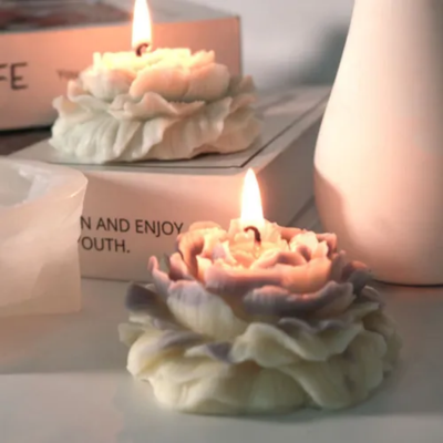 Vela decorativa em forma de flor com pétalas brancas e roxas acesa