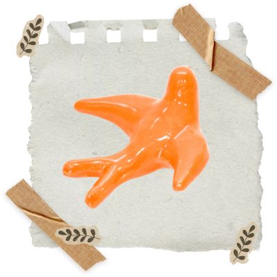 Objeto laranja em forma anatómica sobre fundo de papel cinza claro com fitas de papel e desenhos de ramos