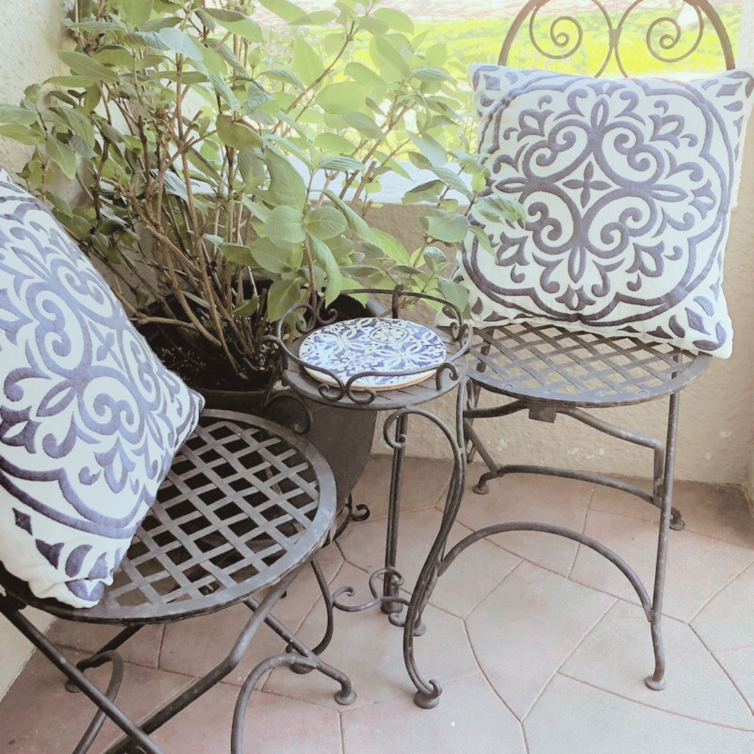 Conjunto de cadeiras de ferro com almofadas decorativas e mesa com prato azul e branco