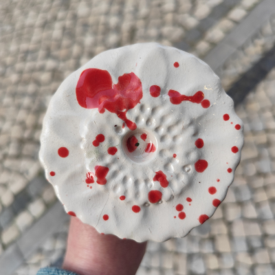 Objecto cerâmico branco com manchas vermelhas sobre uma calçada portuguesa.