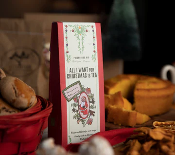 Pacote de chá vermelho com etiqueta branca decorada, rodeado de comida de Natal