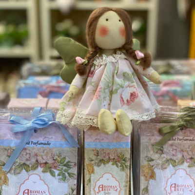 Boneca de pano com vestido florido sentada sobre caixas decoradas de perfumes