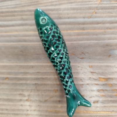 Peixe decorativo de cerâmica verde com textura em relevo sobre madeira clara