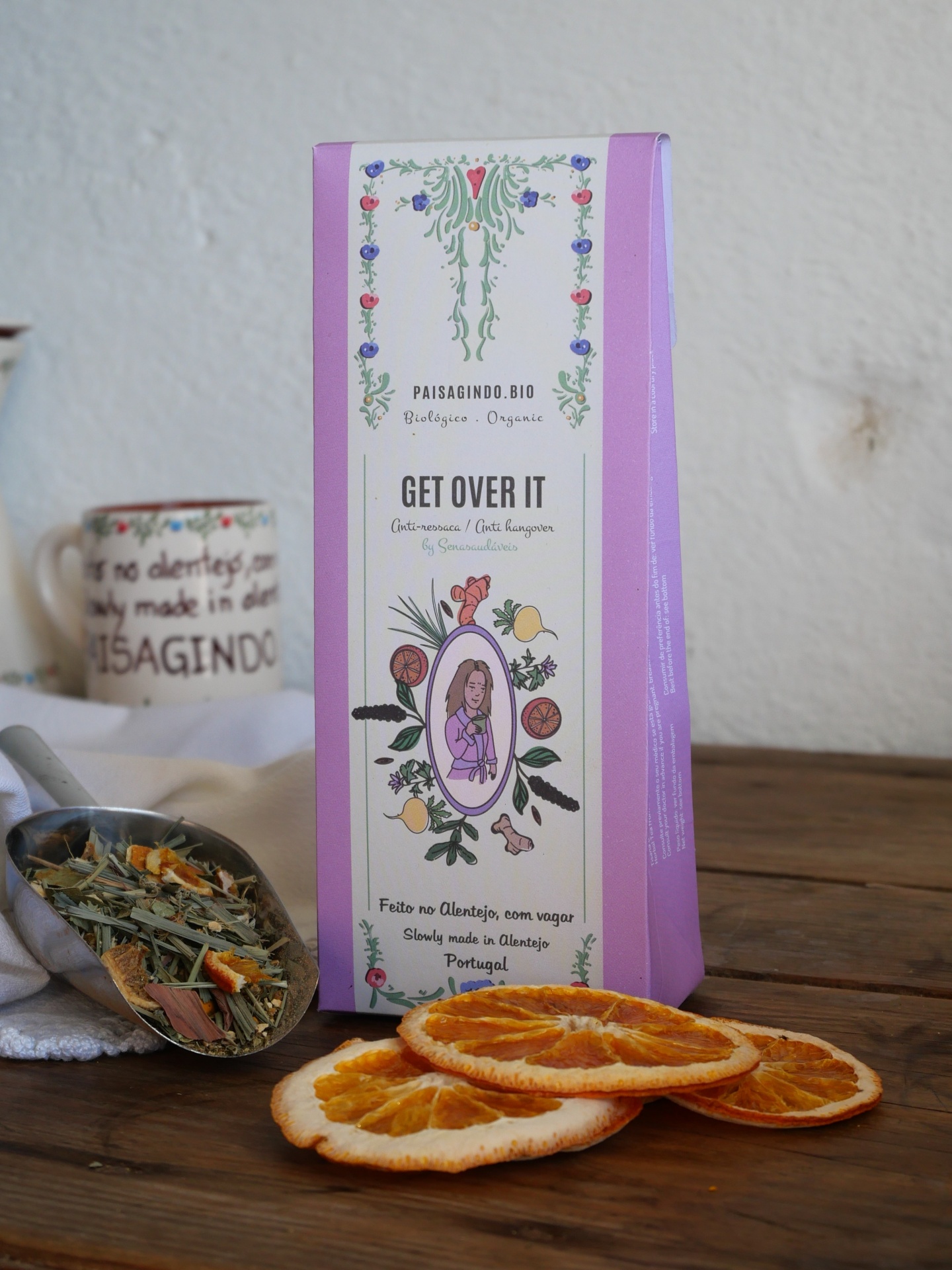 Embalagem de chá orgânico rosa e branco com fatias de laranja desidratada numa mesa de madeira