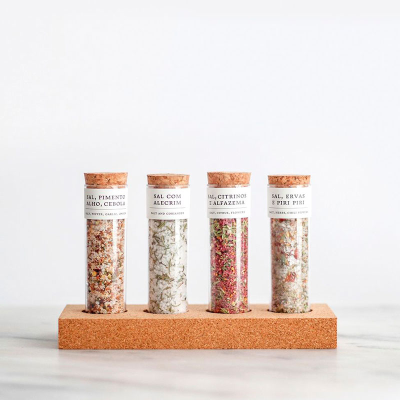 Conjunto de frascos de vidro com sal aromatizado em diferentes cores e texturas, tampas de cortiça, base de cortiça