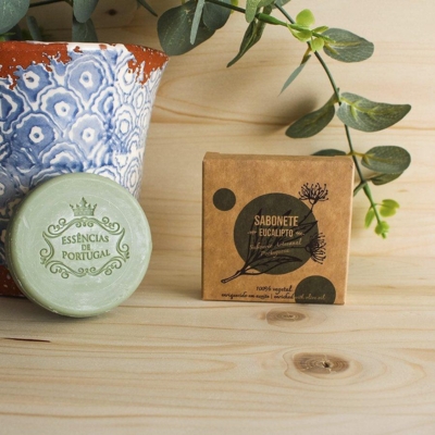 Sabonete redondo verde e embalagem de sabonete de papel castanho com vaso decorativo azul e branco e folhas verdes ao fundo