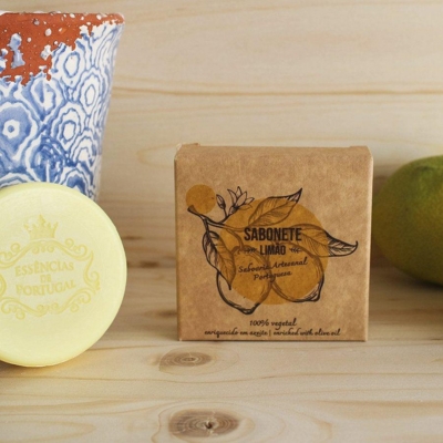 Sabonete de limão embalado em papel kraft com ilustração e texto, sabonete amarelo e jarro azul em superfície de madeira.