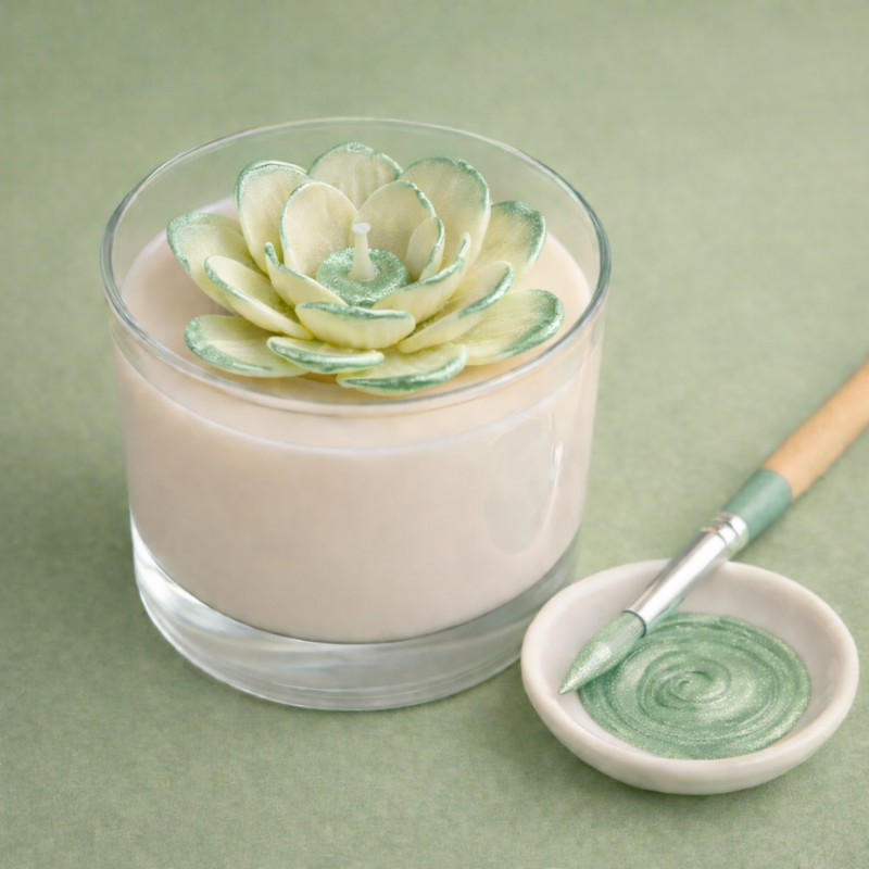 Vela em copo de vidro com flor decorativa creme e verde e pincel com tinta verde em prato branco