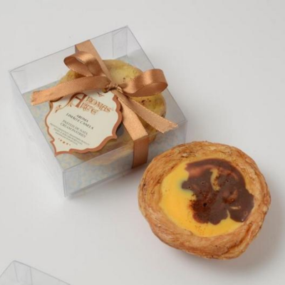 Dois pastéis de nata, um embalado com fita e rótulo e outro fora da embalagem