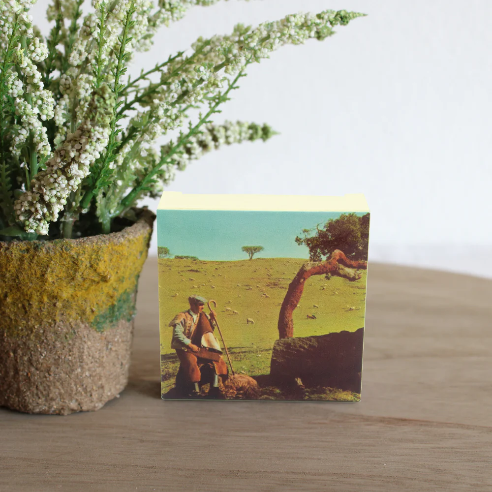 Bloco de notas com imagem de pastor e vaso de flores numa mesa de madeira