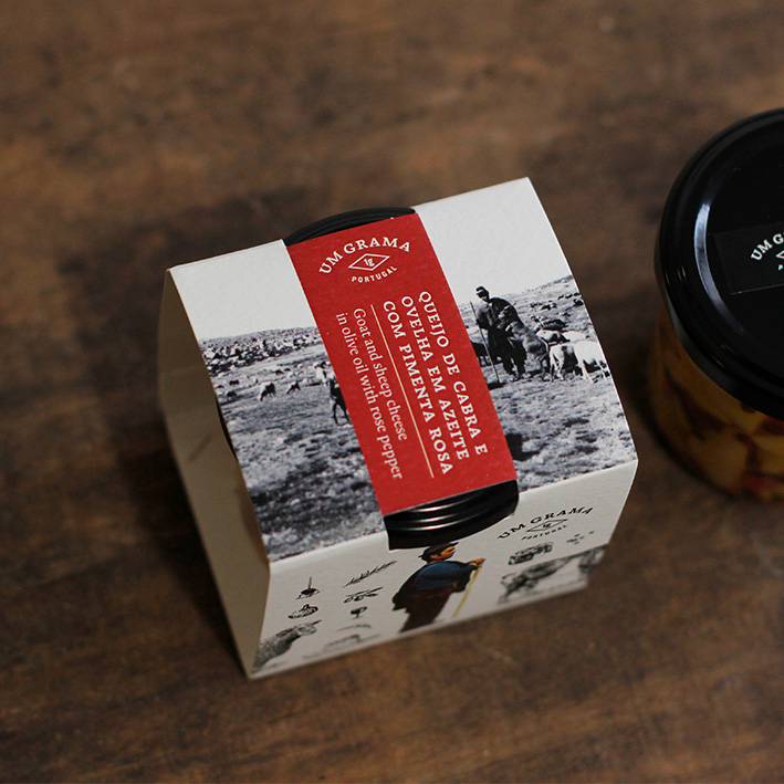 Embalagem de papel cartonado branca com texto vermelho e frasco de vidro com tampa preta em cima de madeira