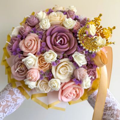 Buquê de flores artificiais com coroa dourada e fita, contra fundo claro.