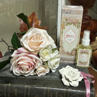 Ramo de flores artificiais rosa e branco com caixa e frasco de spray Aromas Delic Garden sobre livros