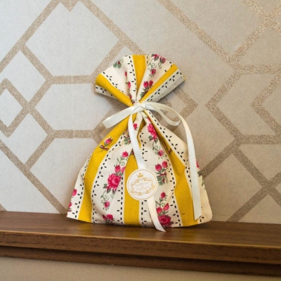 Saco de tecido estampado com riscas amarelas e flores rosas amarrado com fita branca