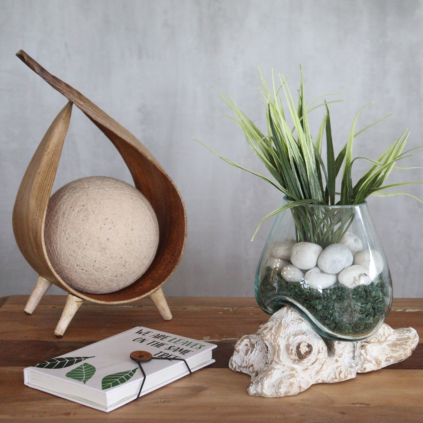 Objetos decorativos em madeira, vidro e planta artificial num ambiente minimalista